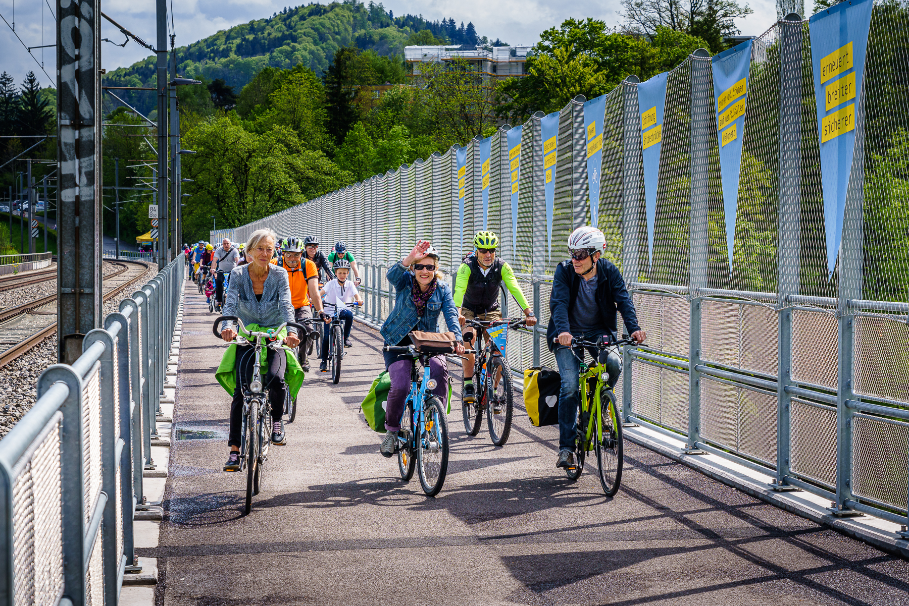 Eine grosse Gruppe Velofahrende fährt über die neue Velobrücke entlang einer Bahnstrecke.